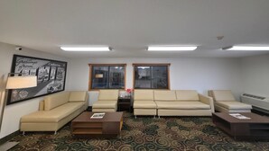 A room with two sofas, a coffee table, a lamp, a framed picture, and a patterned carpet. - Super 8 by Wyndham Coshocton Roscoe Village (Coshocton)