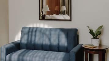 A hotel room with a bed, a blue sofa, a small table with a plant, and a mirror on the wall.