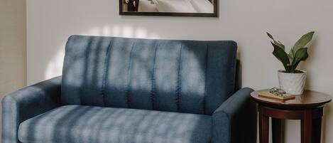 A hotel room with a bed, a blue sofa, a small table with a plant, and a mirror on the wall.