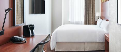 Habitación de hotel con cama, escritorio, silla, teléfono, televisión y cortinas.