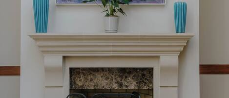 A fireplace with a painting above it, two vases on either side, and a potted plant in the center.