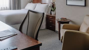 A hotel room with a bed, desk, chair, TV, and artwork on the wall.