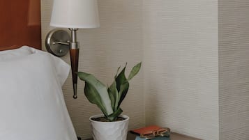 A neatly made bed with white linens, a bedside table with a lamp, a potted plant, and a book.
