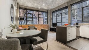 A modern kitchen with a round dining table, grey upholstered chairs, and a brick accent wall. - Punthill Manhattan (Melbourne)