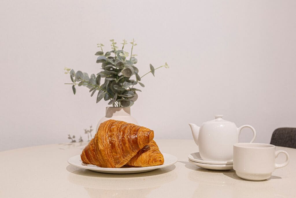A table with a croissant, a teapot, and a cup, accompanied by a small plant.