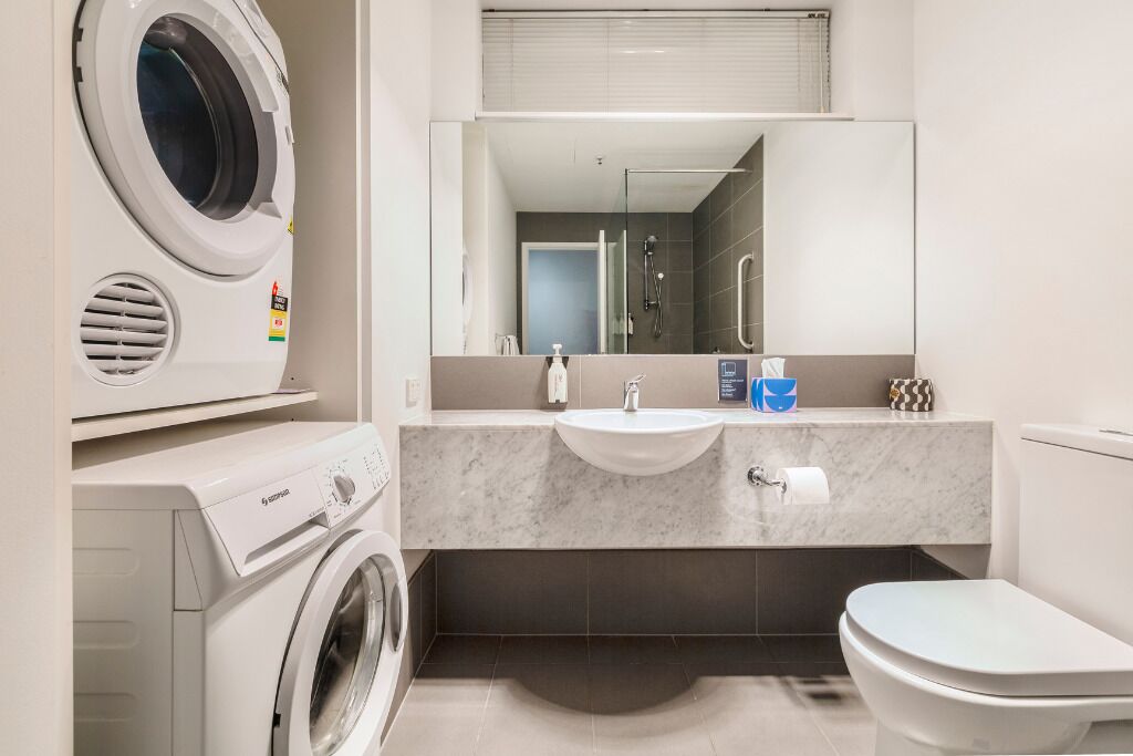 Un baño moderno con lavadora incorporada, un lavamanos, un espejo y un inodoro.