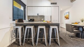 A modern kitchen with white cabinets, a granite countertop, and a central island with stools. - Punthill Manhattan (Melbourne)