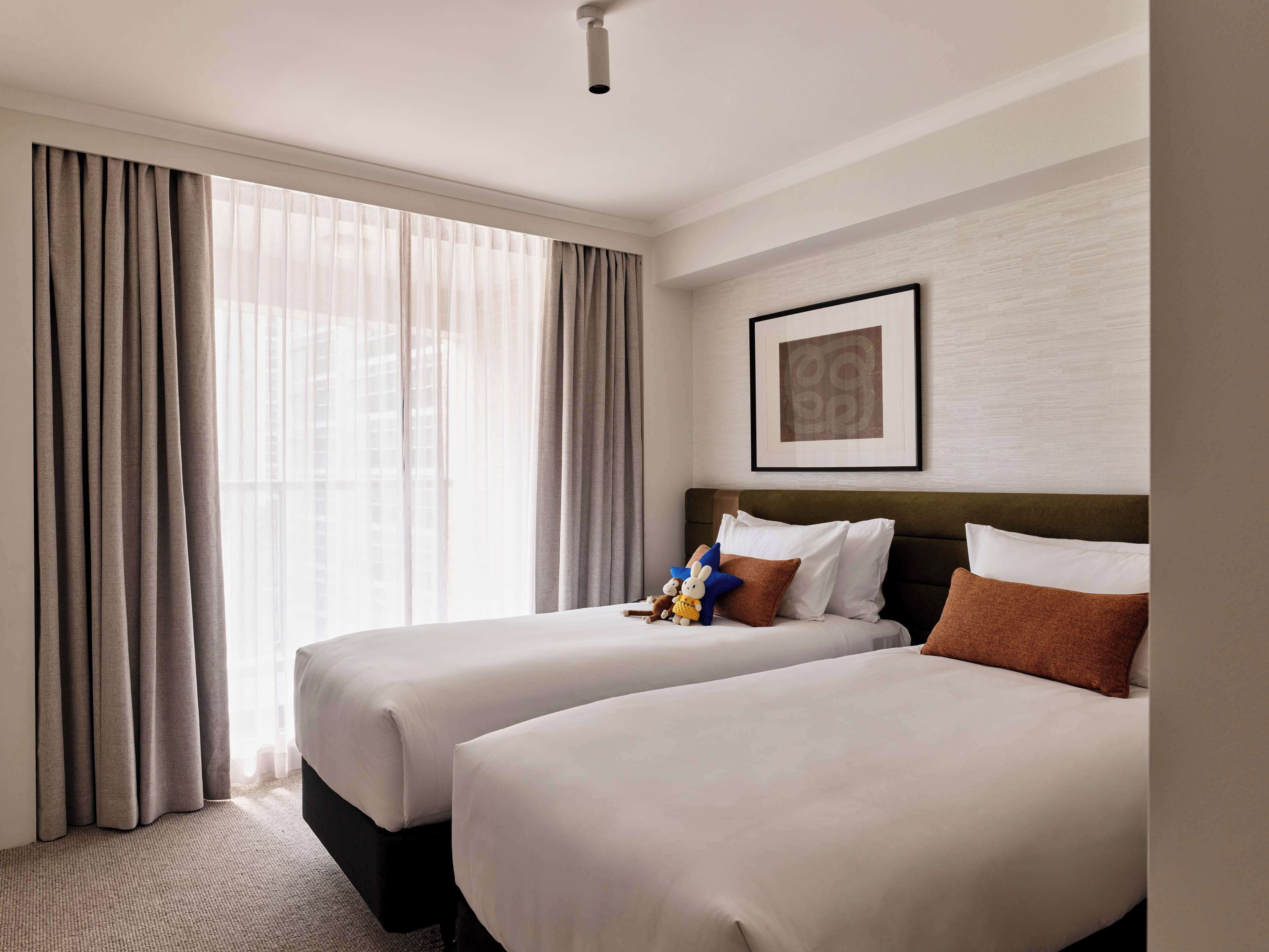 A hotel room with two beds, a framed picture on the wall, and a window with curtains.