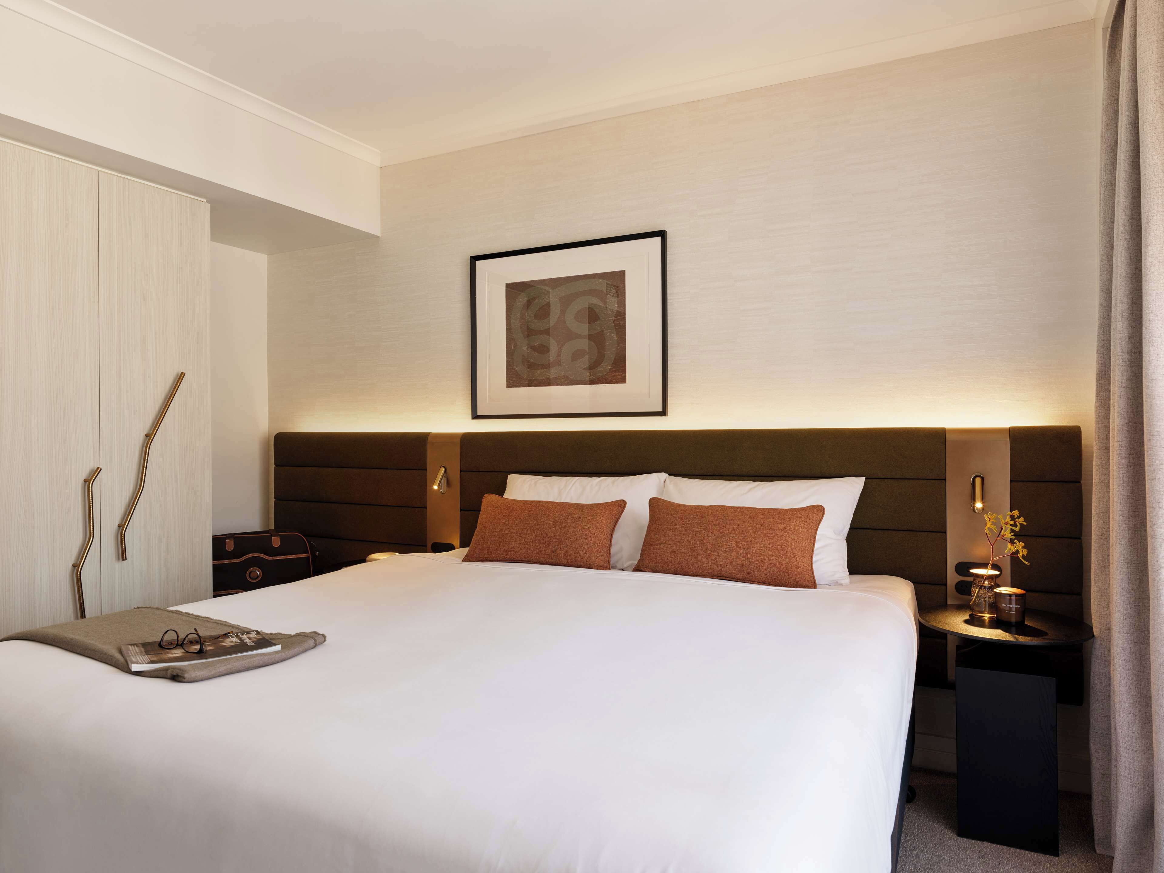 A hotel room with a large bed, a bedside table with a lamp, a framed artwork on the wall, and a door with a towel rack.