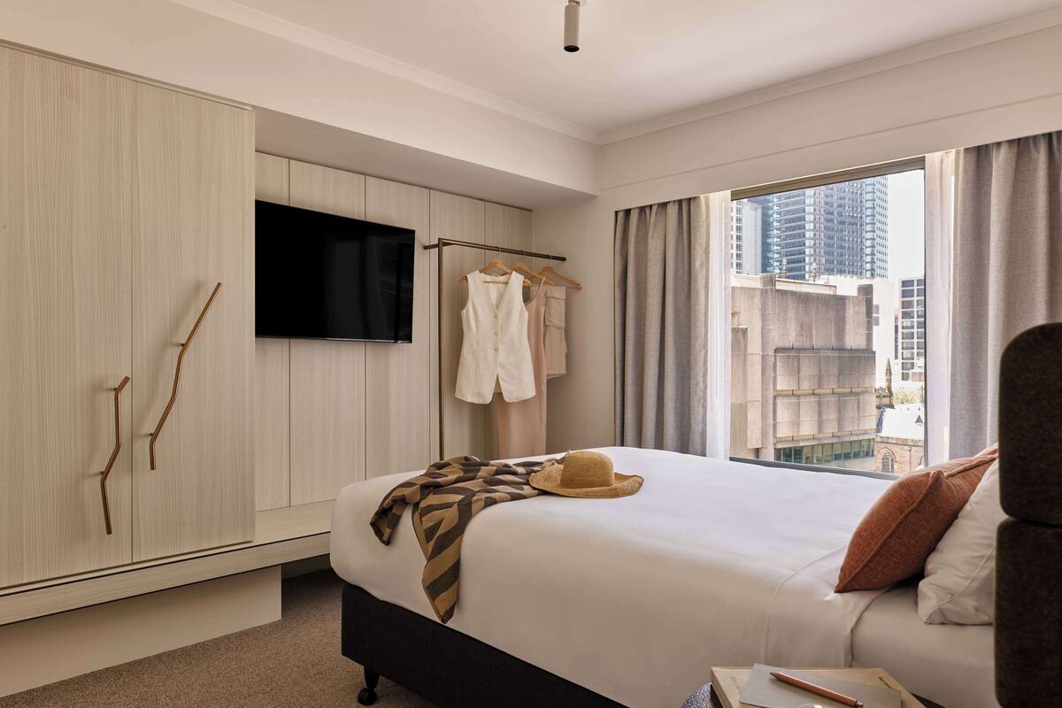 Habitación de hotel con cama, televisión, armario y vista a la ciudad.