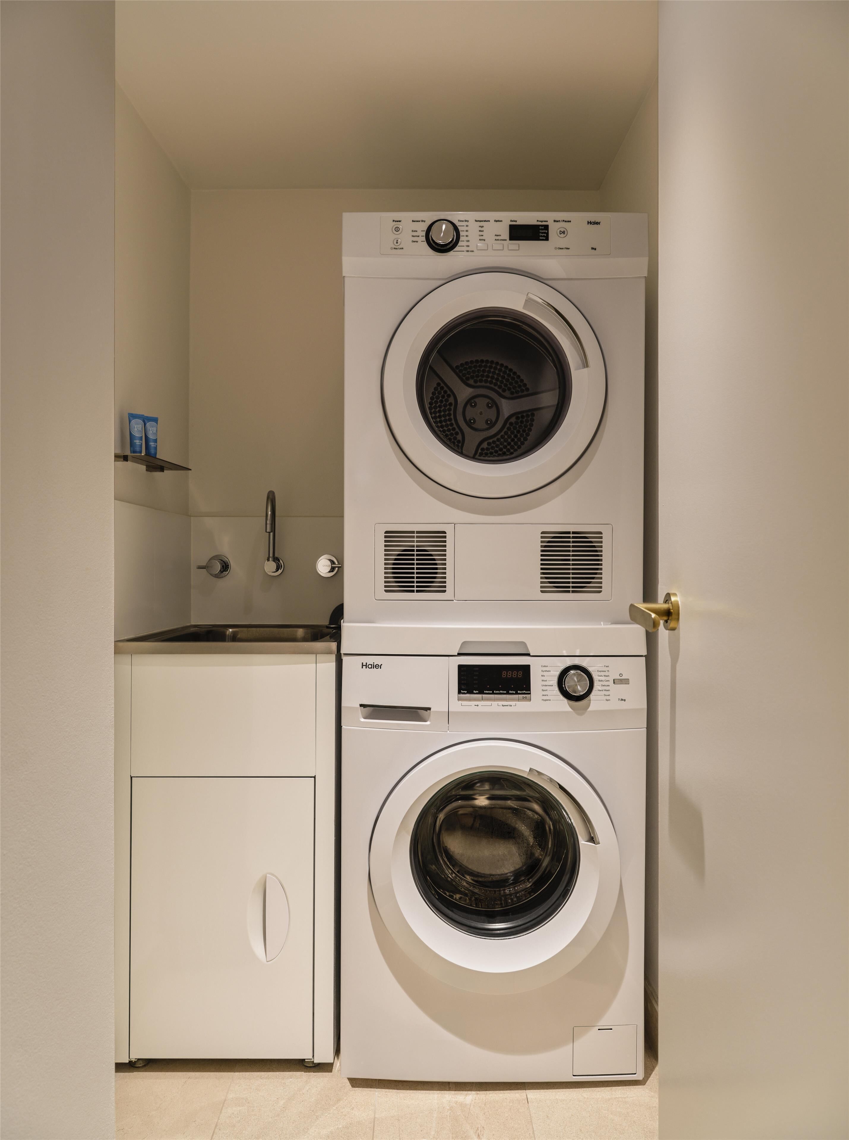 Ein kleiner Hauswirtschaftsraum mit übereinander gestapelten Waschmaschine und Trockner, einem kleinen Waschbecken und einem Schrank.