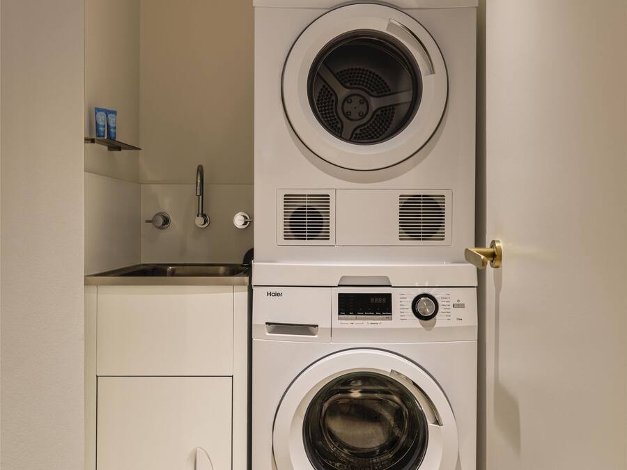 Ein kleiner Hauswirtschaftsraum mit übereinander gestapelten Waschmaschine und Trockner, einem kleinen Waschbecken und einem Schrank.