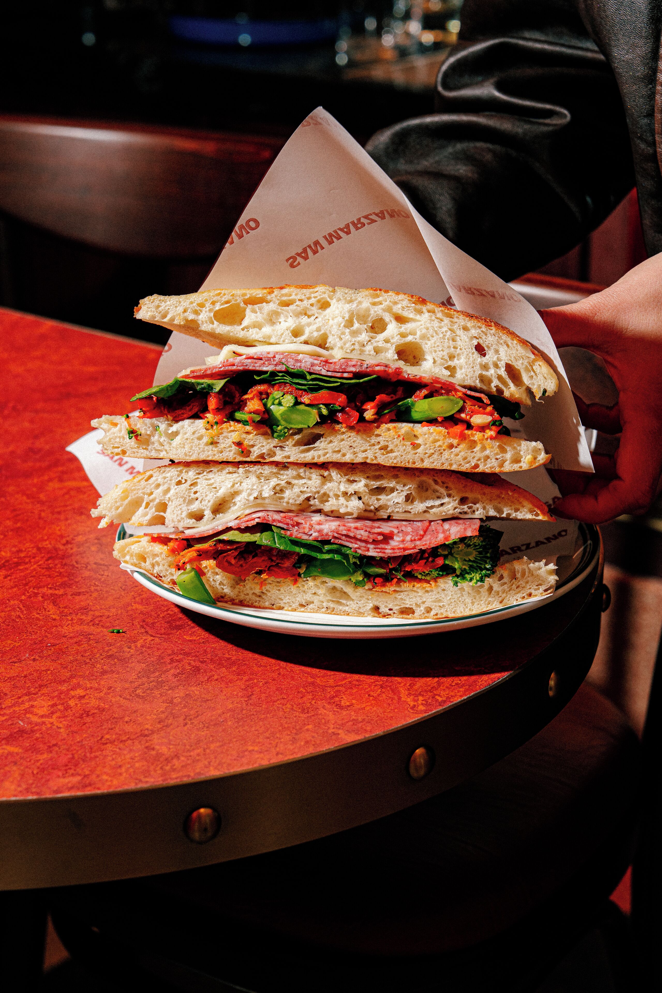 A sandwich on a plate with a paper wrapper.