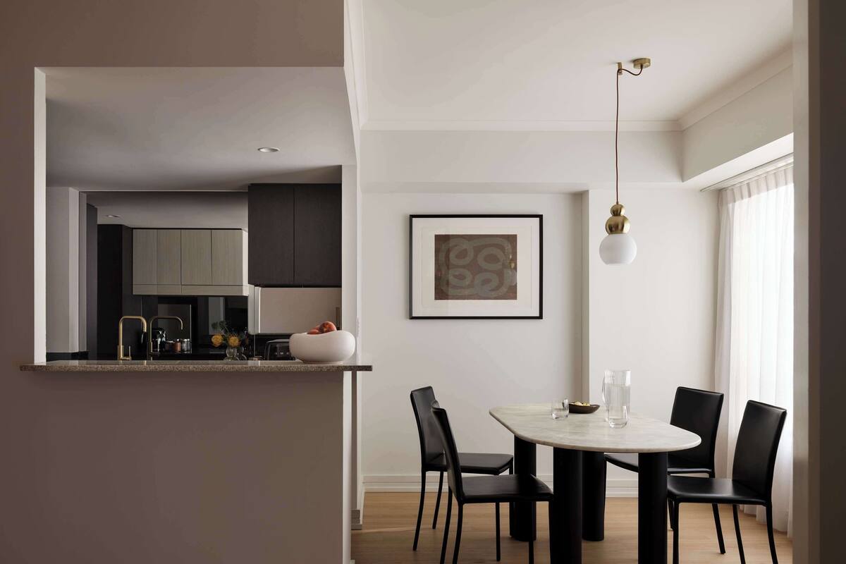 Una cocina moderna con armarios oscuros, encimera blanca y una zona de comedor con una mesa redonda y sillas negras.