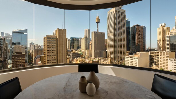 A modern room with a round marble table, large windows with a city skyline view, and a curved ceiling.