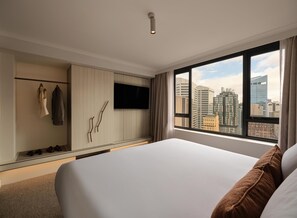 A hotel room with a bed, a TV mounted on the wall, a wardrobe, and a view of the cityscape through large windows. - Adina Sydney Town Hall (Sydney)