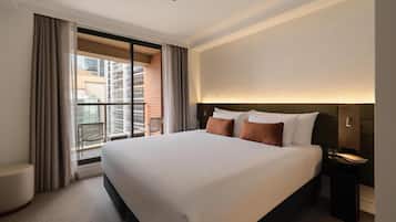 A hotel room with a large bed, a nightstand, a chair, and a view of a cityscape through a balcony.