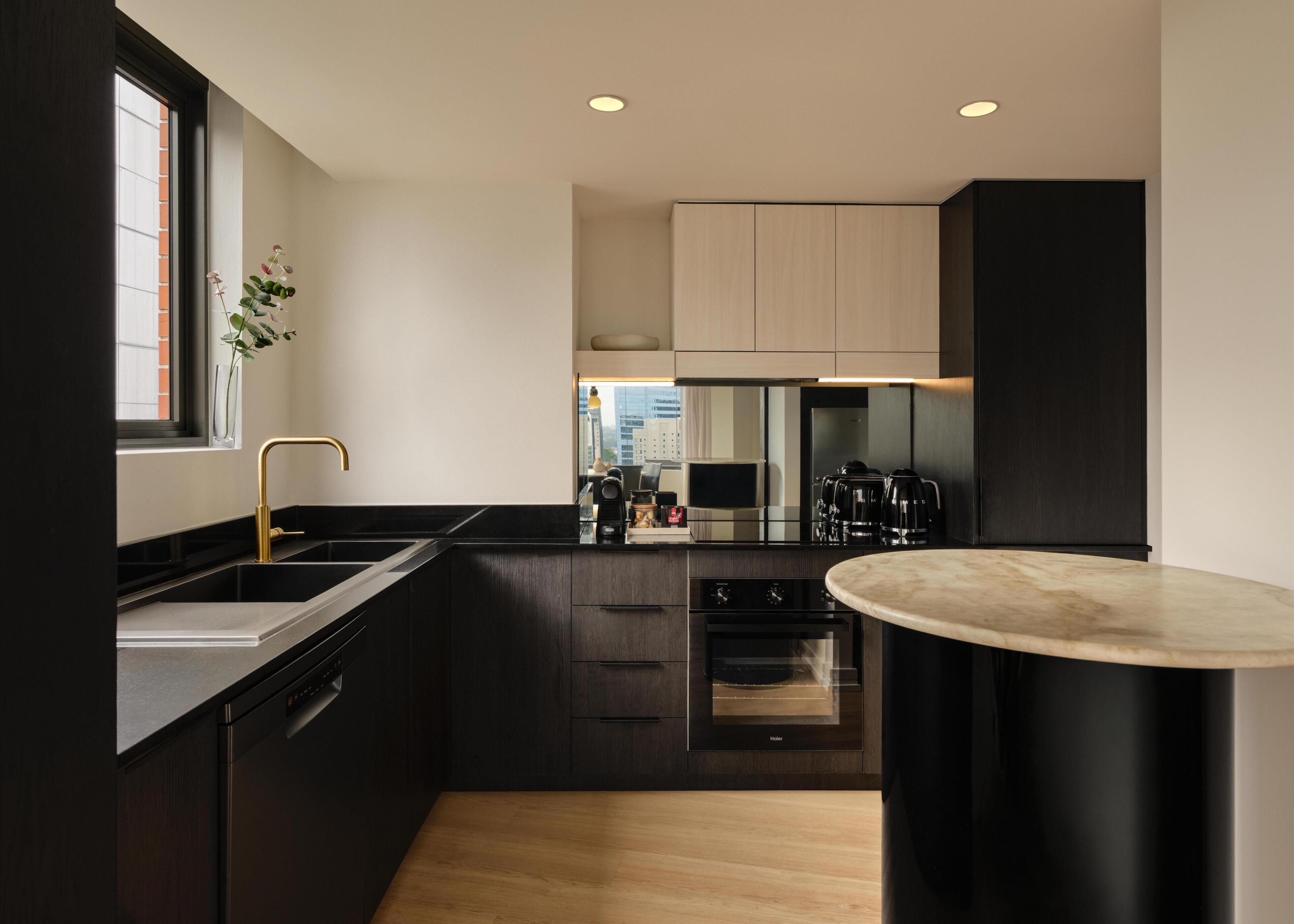 A modern kitchen with dark cabinetry, a stainless steel sink, a built-in oven, and a round marble countertop.