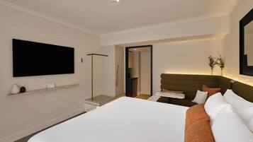 Quarto de hotel com uma cama grande, televisão de tela plana na parede, mesa de cabeceira e porta de acesso a um banheiro.