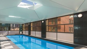 Une piscine intérieure dotée d’un sol à carreaux, de grandes fenêtres et d’un design moderne au niveau du plafond.