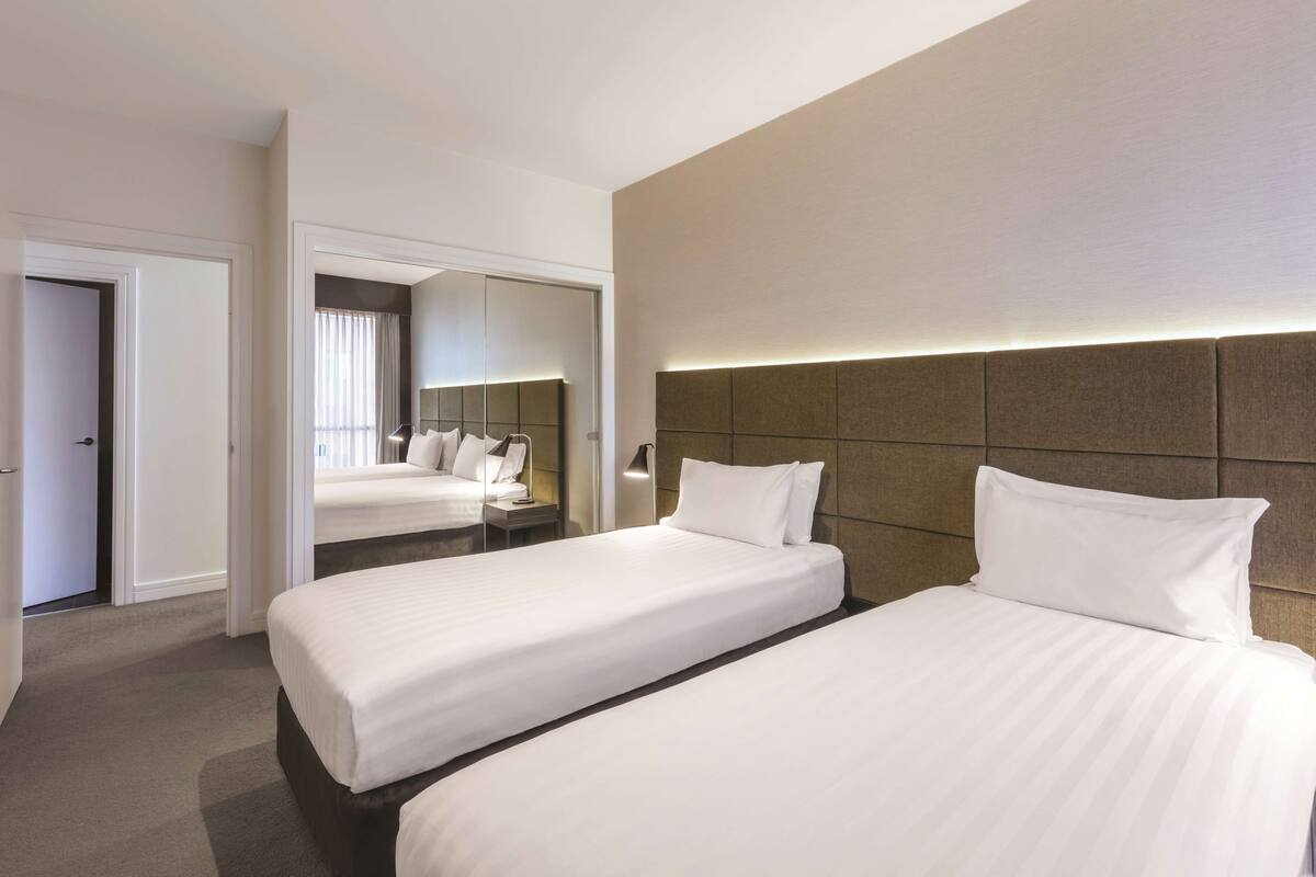 A hotel room with two beds, a large mirror, and a modern headboard.