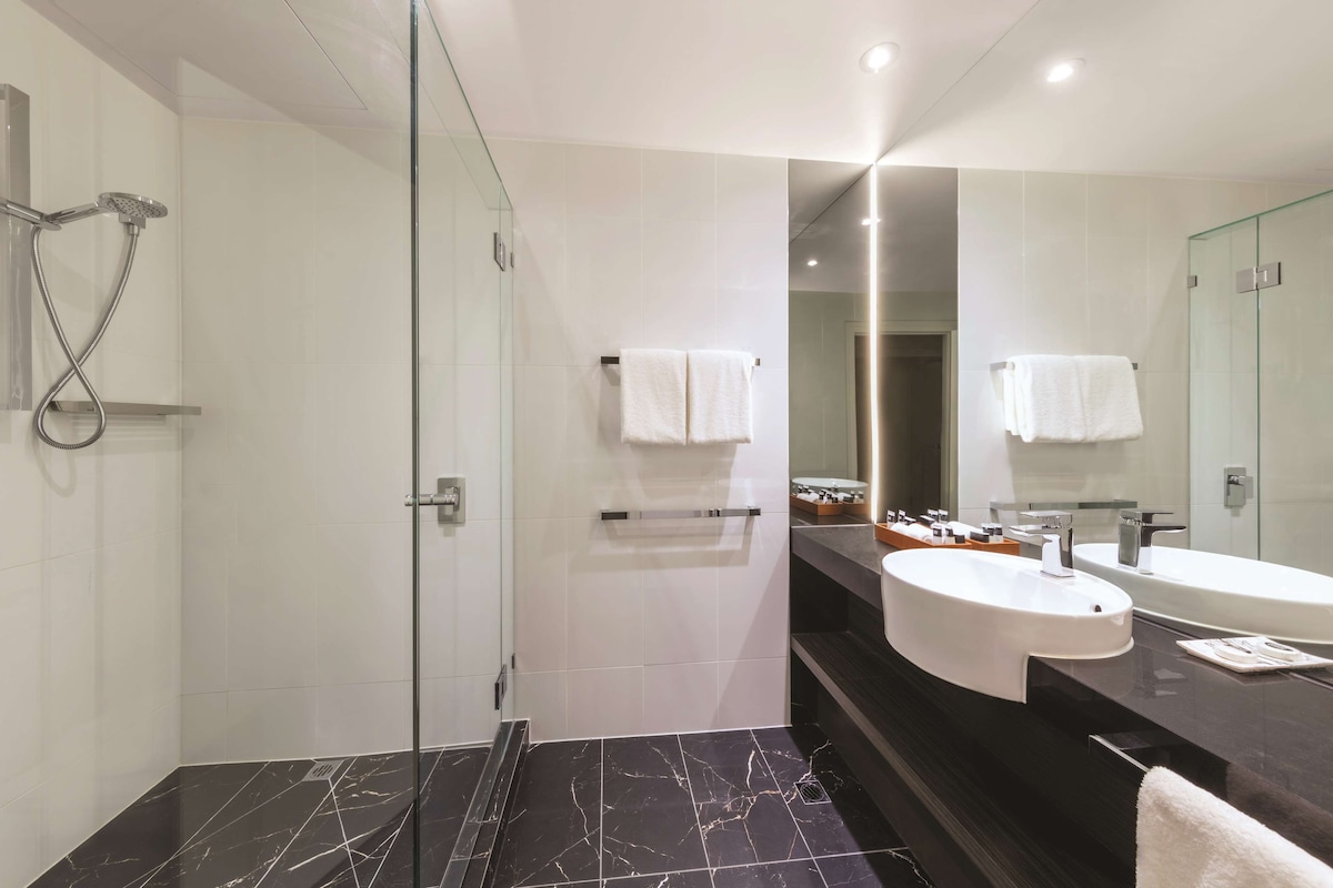 Een moderne badkamer met een douche met glazen wand, twee wasbakken en een grote spiegel.