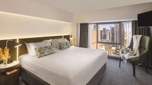 Une chambre d’hôtel avec un grand lit, une vue sur la ville, un fauteuil vert et un téléviseur à écran plat.