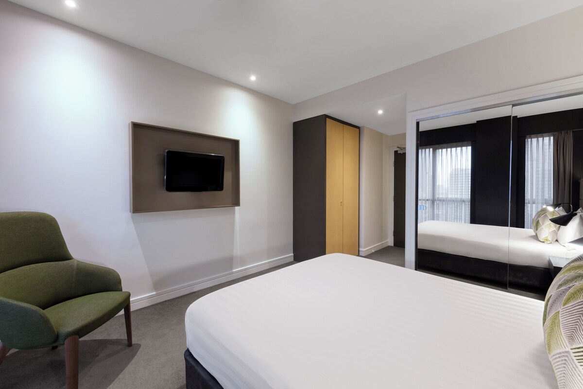 Habitación de hotel con cama, una silla, televisor y puerta corrediza que da a un balcón.