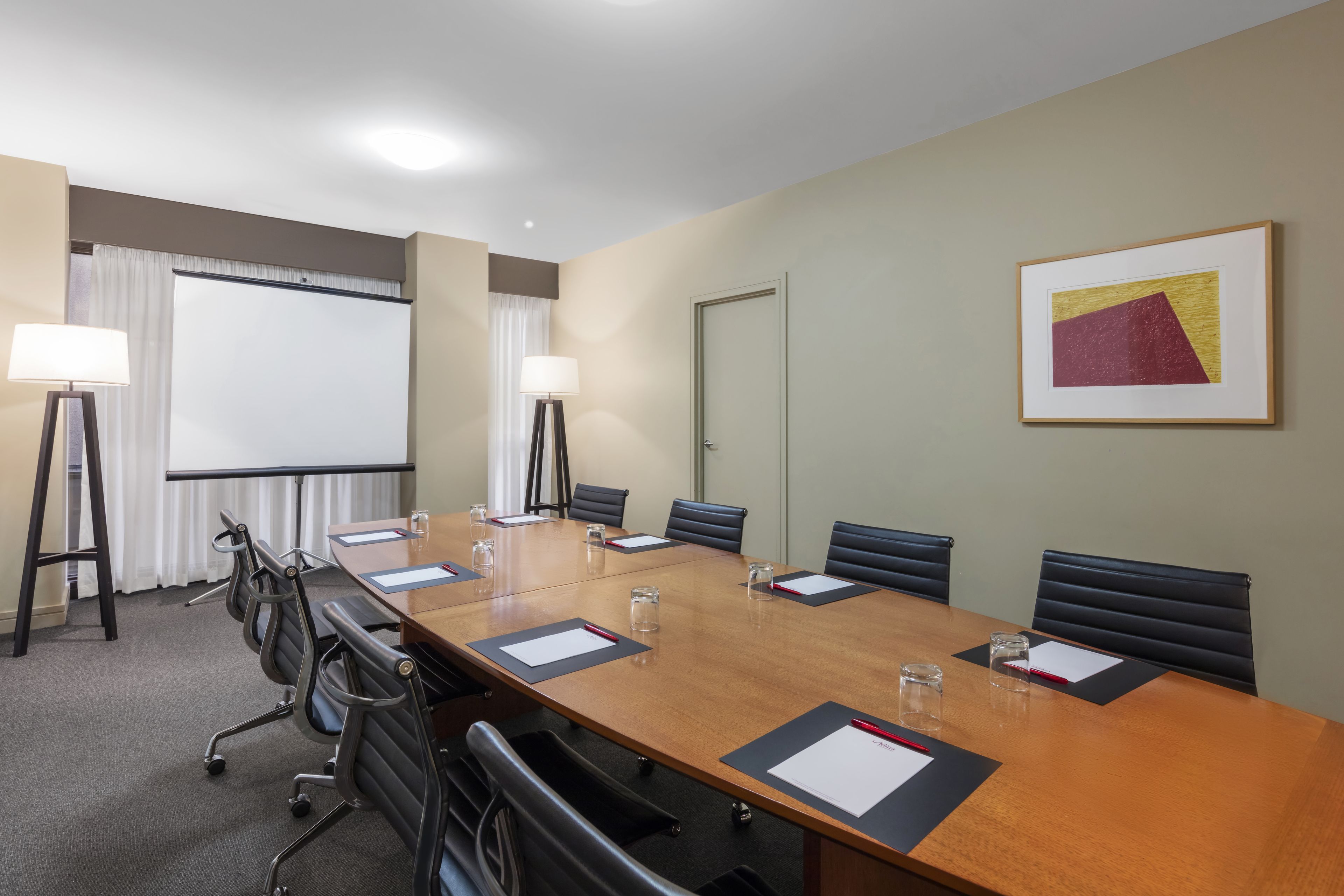 Une salle de conférence avec une longue table, des chaises, un écran de projection et un tableau encadré au mur.