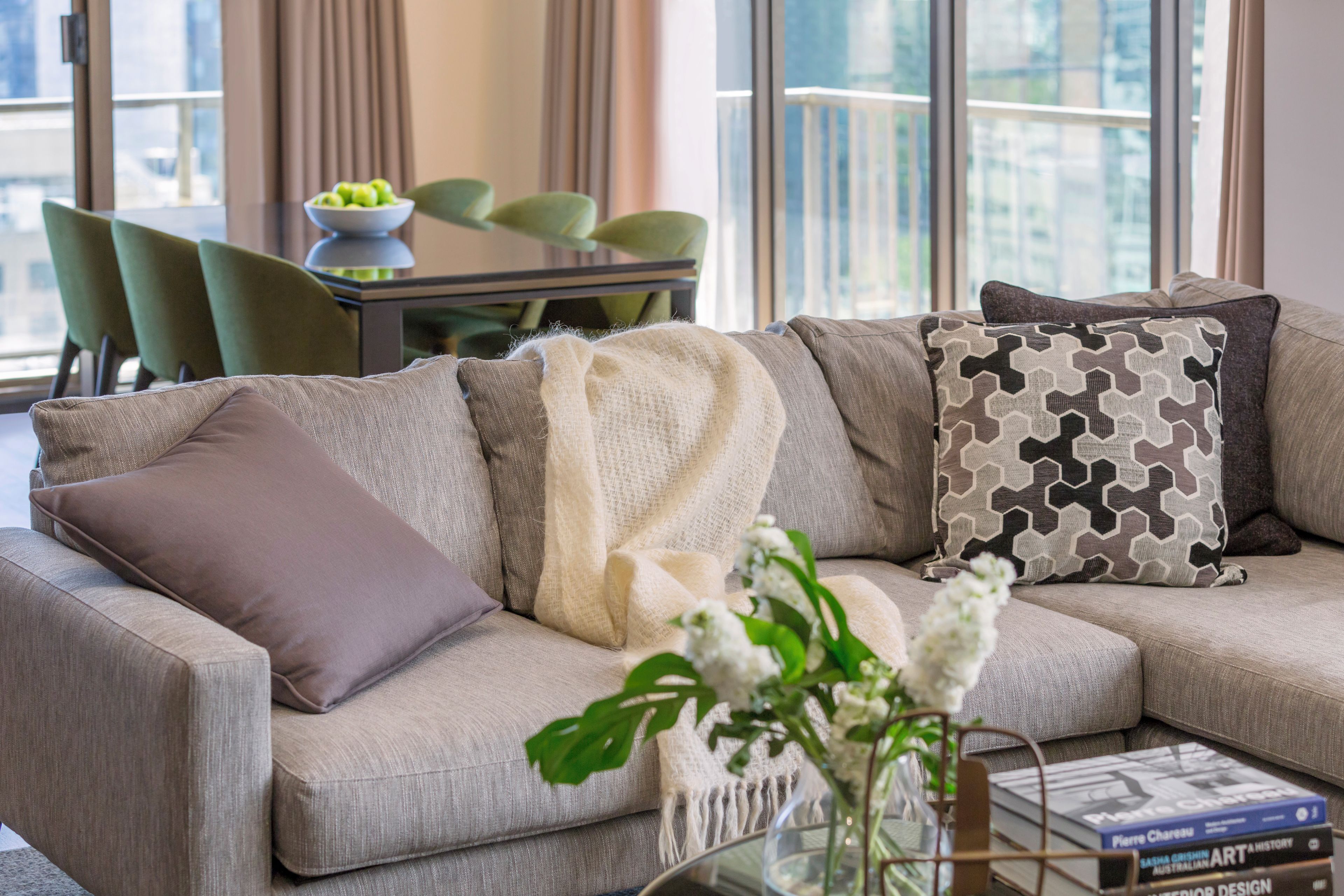 A modern living room with a sectional sofa, a coffee table with books, and a view of the city through large windows.