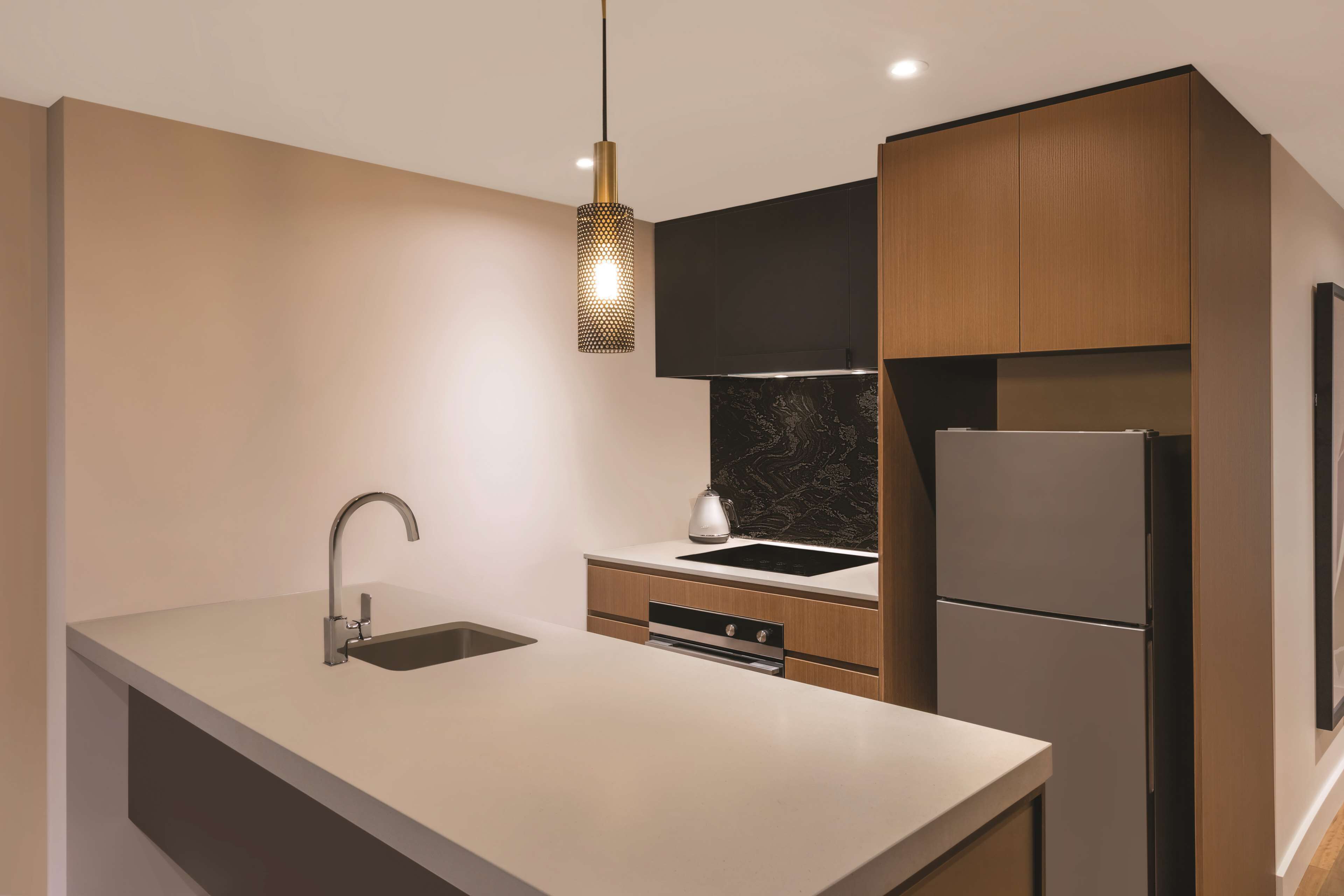 A modern kitchen with a sleek stainless steel refrigerator, a minimalist sink, and a pendant light fixture.
