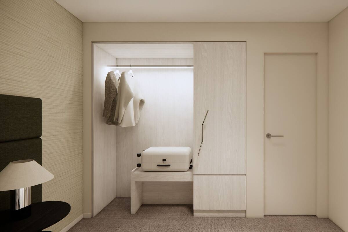A small, neatly organized room with a bed, bedside table, and a closet with hanging clothes.