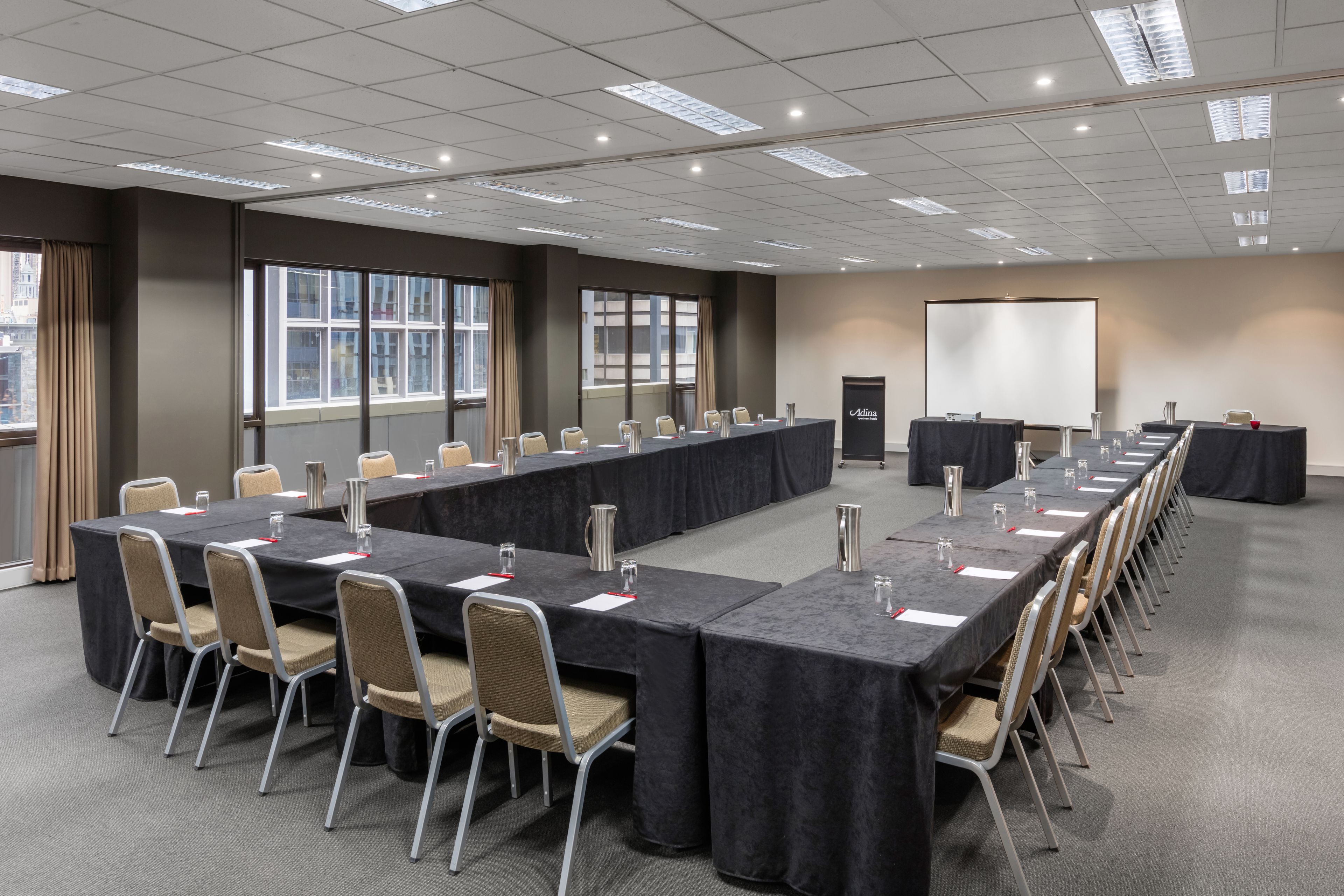 A conference room with a long table, chairs, a projector screen, and a door.