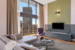 Una sala de estar moderna con un sofá, una mesa redonda de centro, un sillón morado y un televisor sobre una pared gris.
