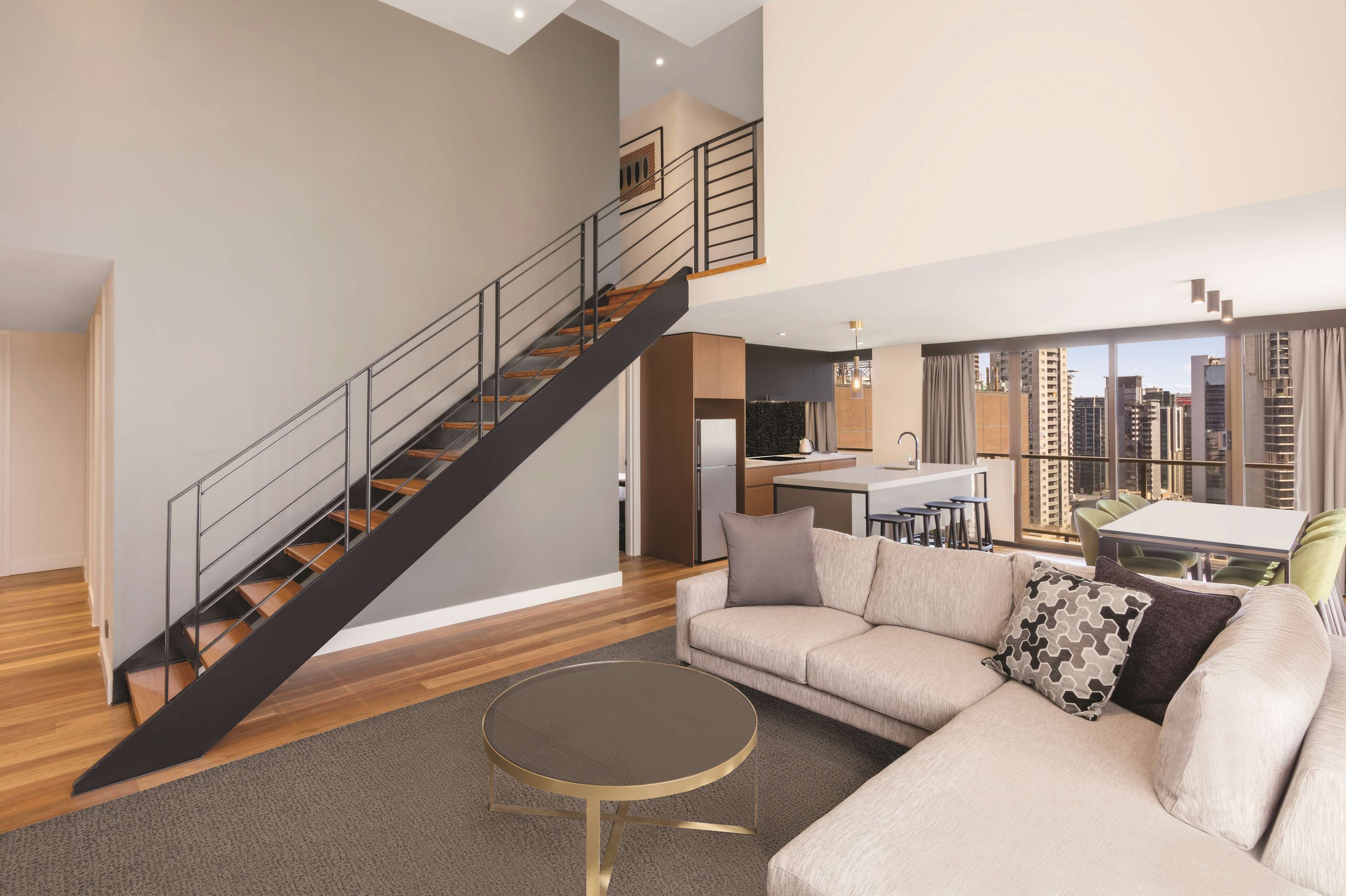 Un apartamento moderno con una escalera, una sala de estar con sofá y una mesa de centro, y una zona de cocina.