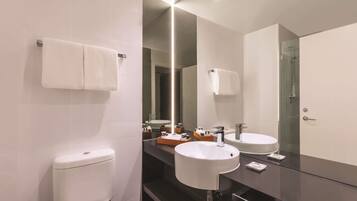 Un baño moderno con inodoro, dos lavamanos, un espejo grande y cabina de ducha de vidrio.