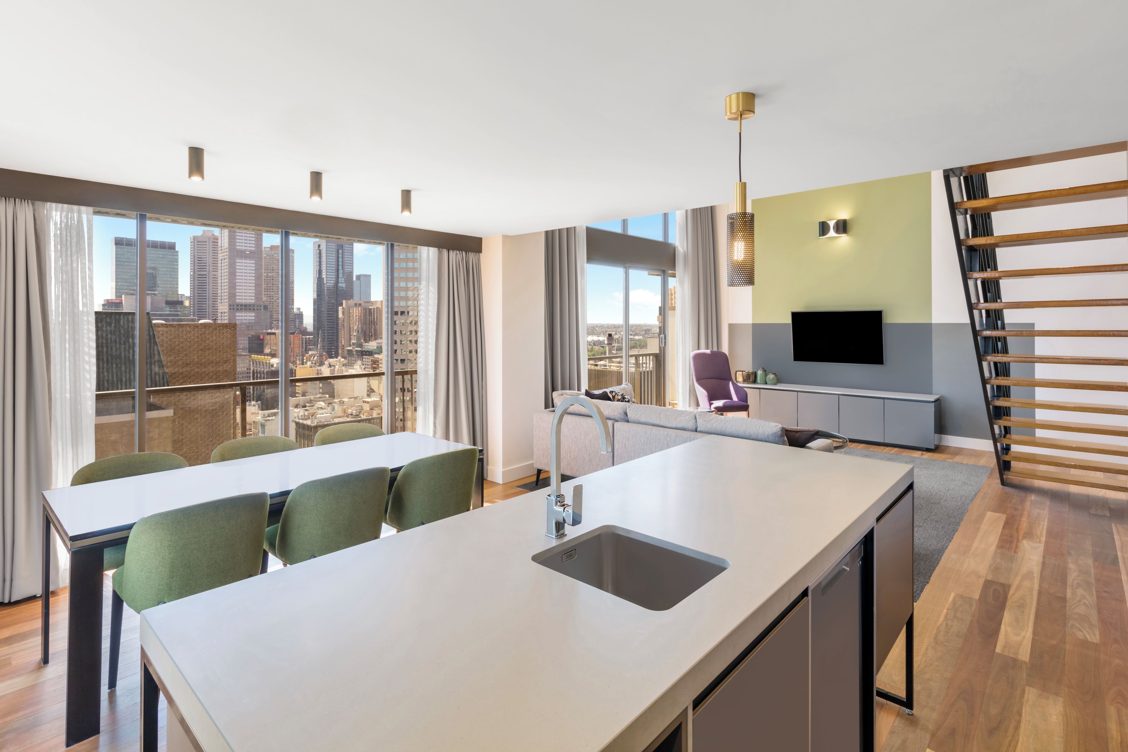 Una cocina moderna con una isla central, un comedor con sillas y un televisor en la pared.