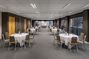 Een vergaderruimte met meerdere ronde tafels, stoelen en een podium.