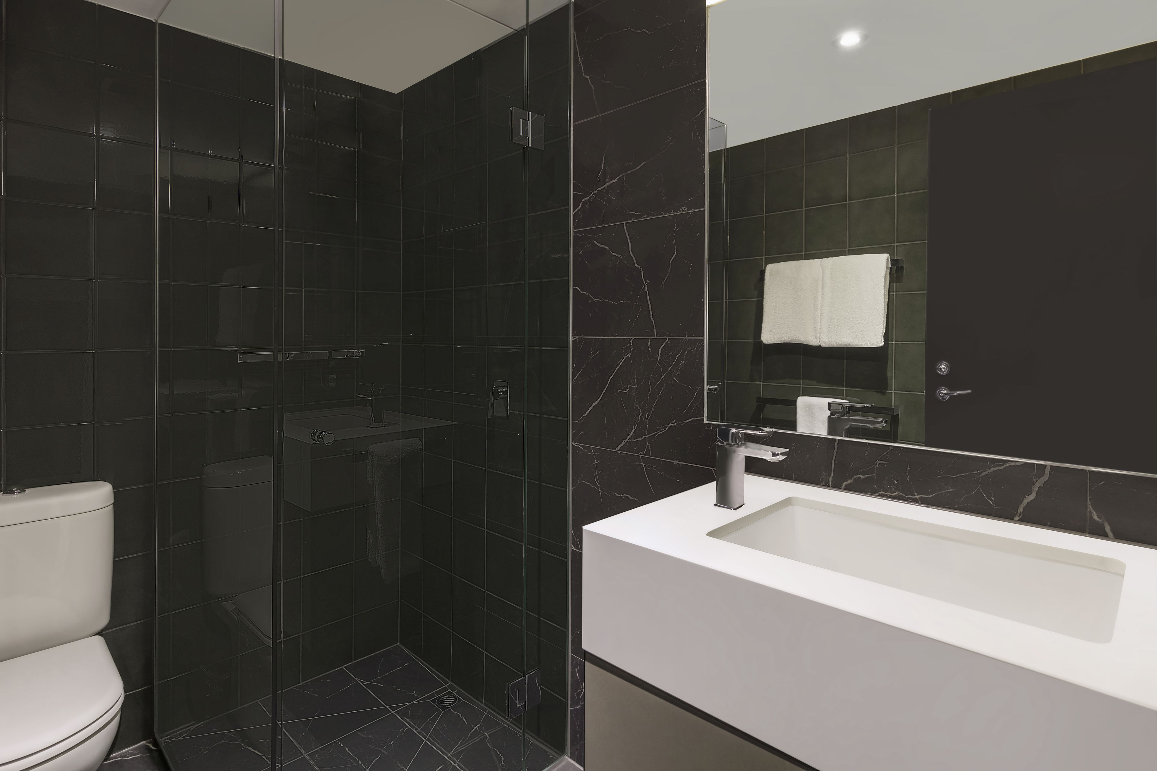 Un baño moderno con ducha separada por vidrio, un lavamanos blanco y un espejo grande.