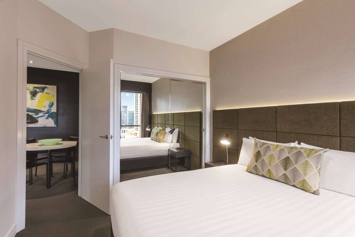 A hotel room with a bed, bedside table, and a dining area with a table and chairs.