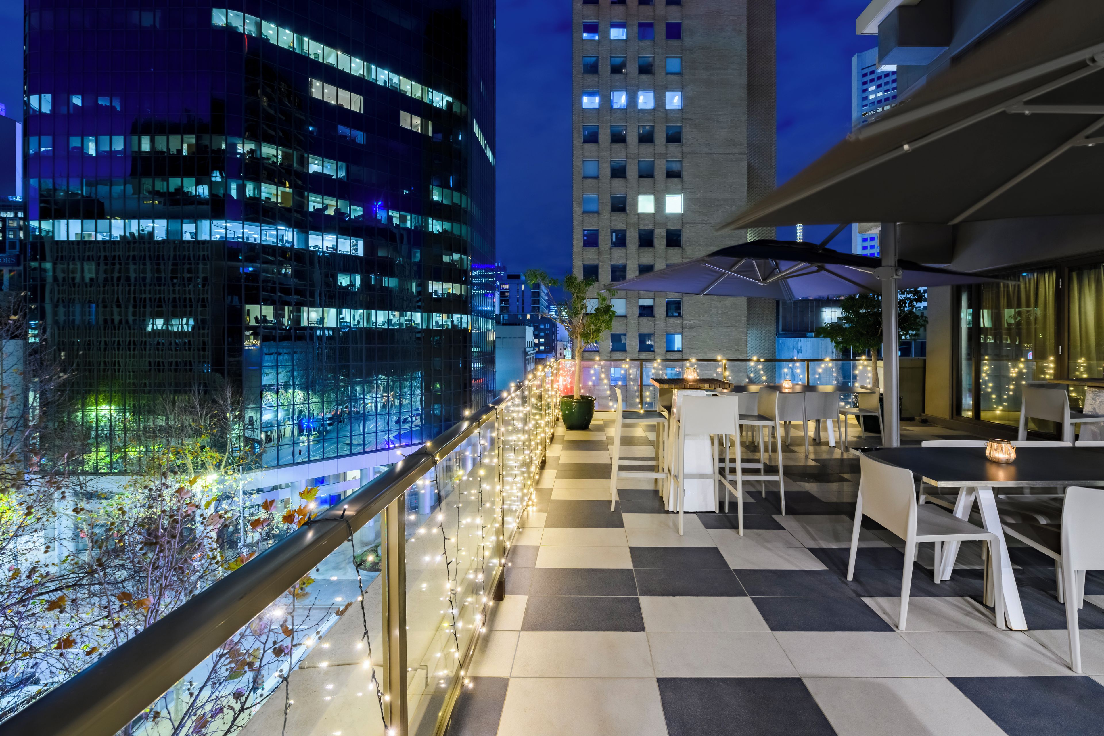 Terraza en la azotea con mobiliario exterior, vista panorámica de la ciudad de noche y un suelo con diseño de cuadros.