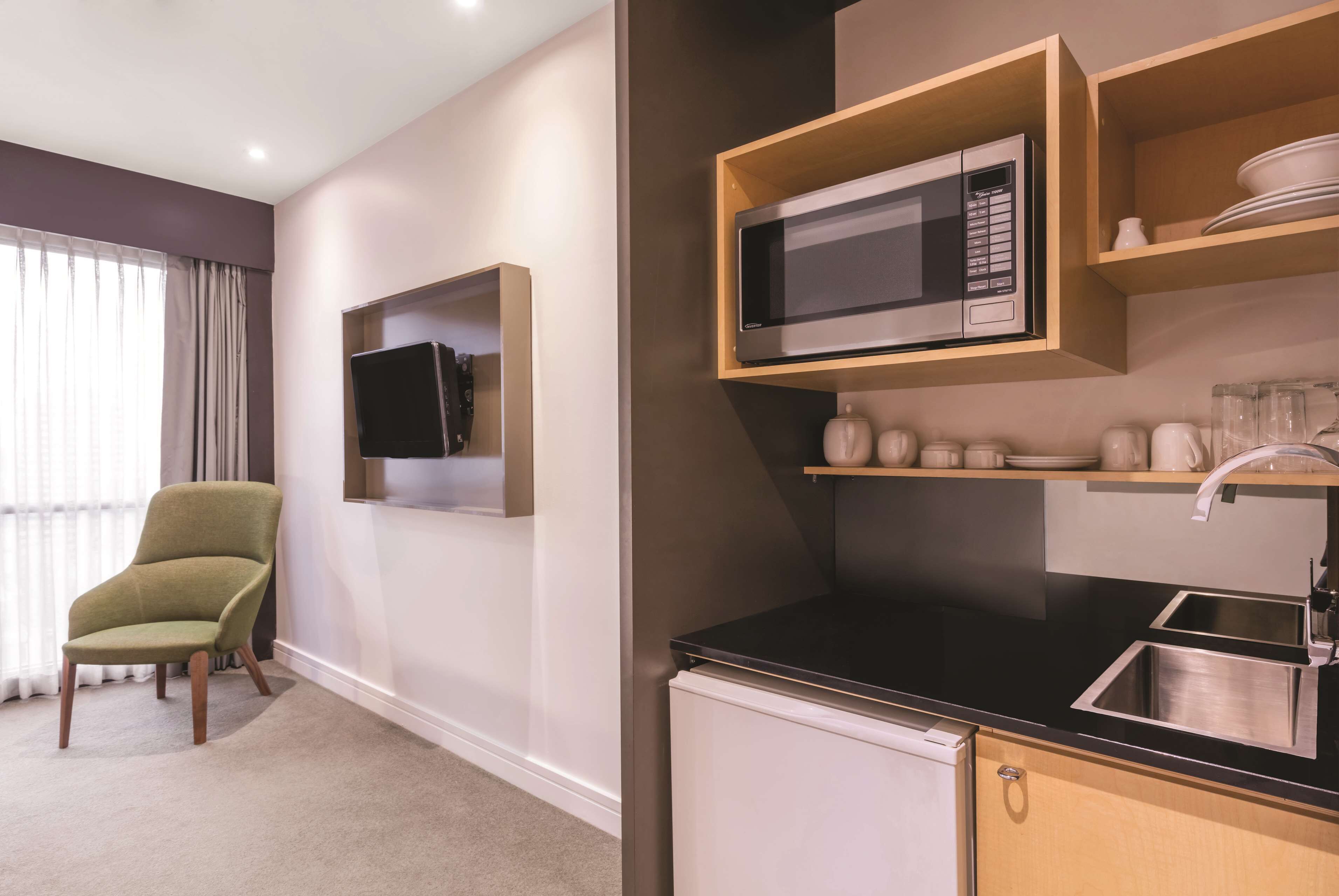A compact kitchen with a microwave, sink, and storage shelves.
