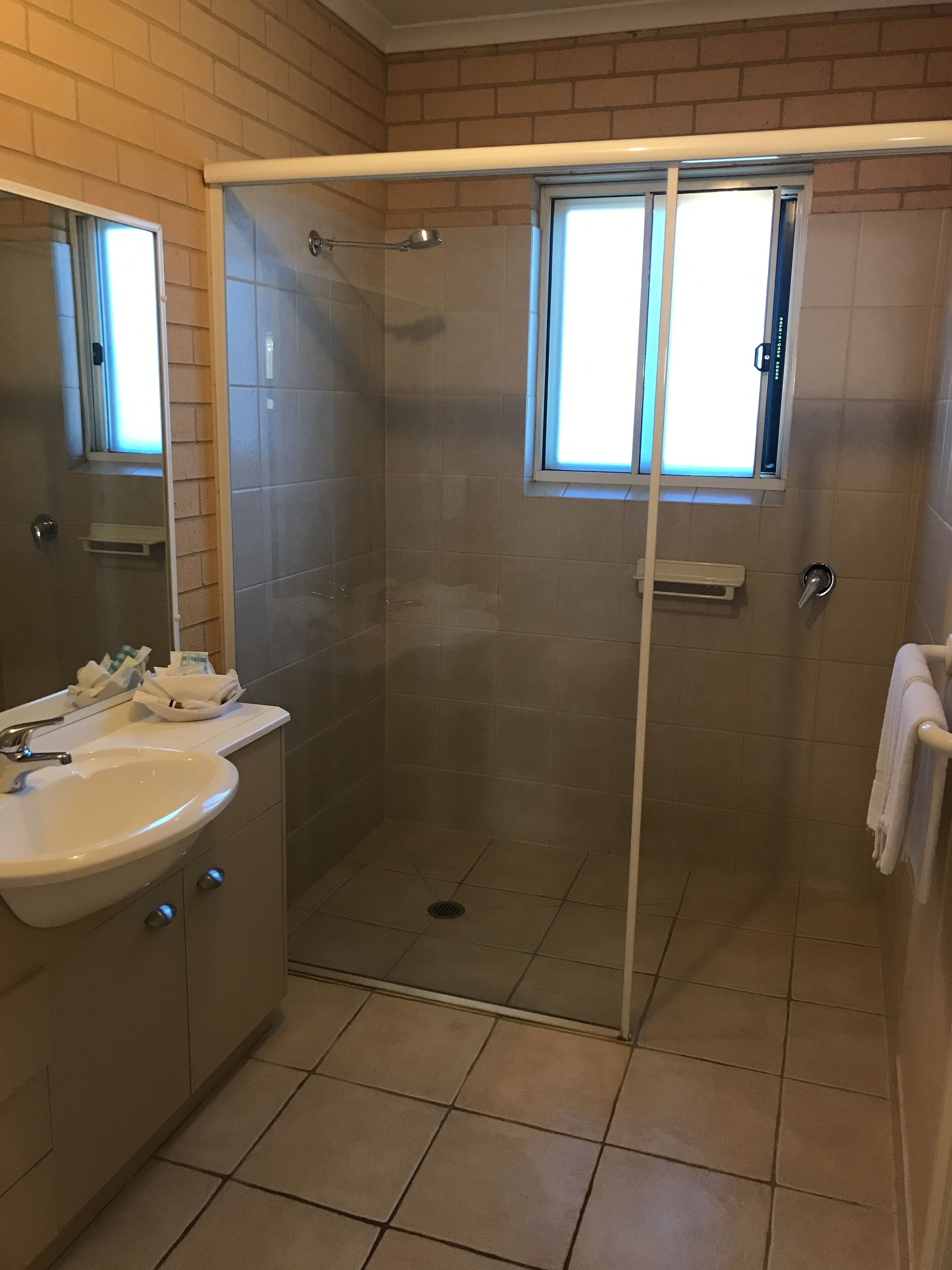 A bathroom with a glass-enclosed shower, a sink, and a window.