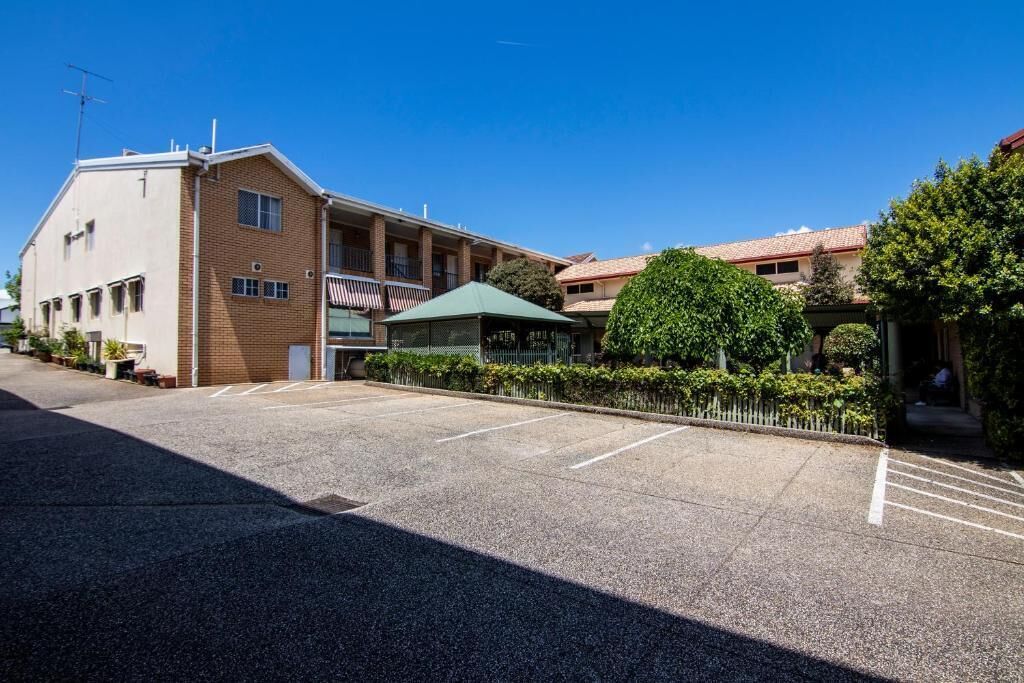 Un edificio con estacionamiento, un área techada y un jardín cercado.