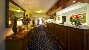 A hotel lobby with a patterned carpet, a reception desk, a large mirror, and a vase with flowers. - Albury Georgian Motel & Suites (Albury)
