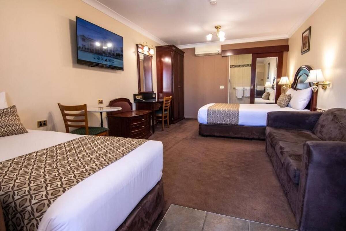 A hotel room with two beds, a desk, a chair, a sofa, a TV, and a mirror.