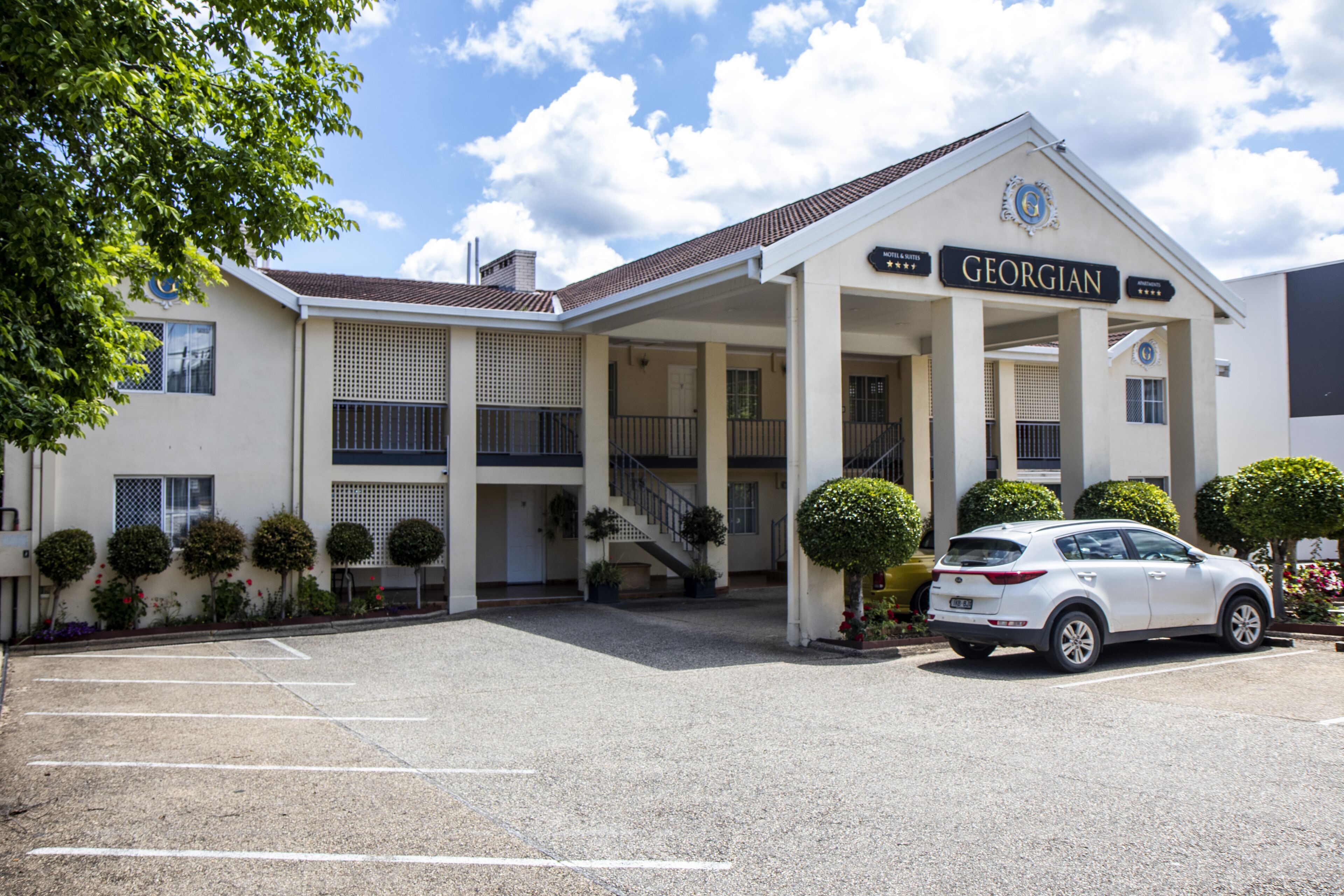 A Georgian hotel with a covered entrance, a parking lot, and a white car parked in front.