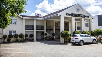 A Georgian hotel with a covered entrance, a parking lot, and a white car parked in front.