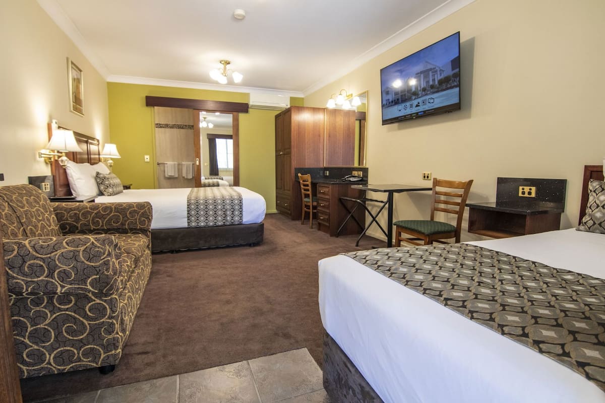 A hotel room with a bed, a desk, a chair, a sofa, and a TV on the wall.