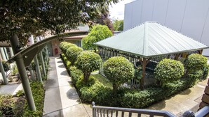 A covered outdoor area with a metal roof, surrounded by neatly trimmed bushes and trees. - Albury Georgian Motel & Suites (Albury)
